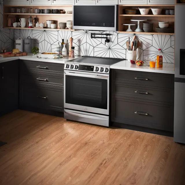 Woman cooking on an LG Range in a kitchen. Group of appliances to the left and text reading “Get $150 Instant Savings”.